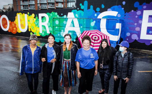 A group of Coast Mental Health's Rabble Rousers (young adults) stand infront of a mural of the word's 'Courage'