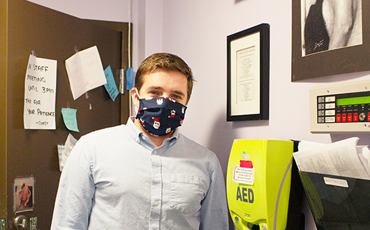 Staff member Jacob stands next to a newly installed AED