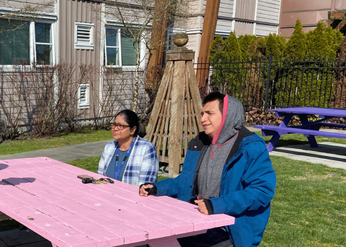 Chris, a client, sits at a pink table with staff member Veena.